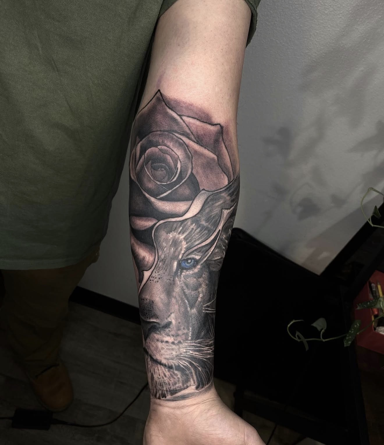 Black and grey realism forearm piece — a rose unfolding into a lion with pale eyes