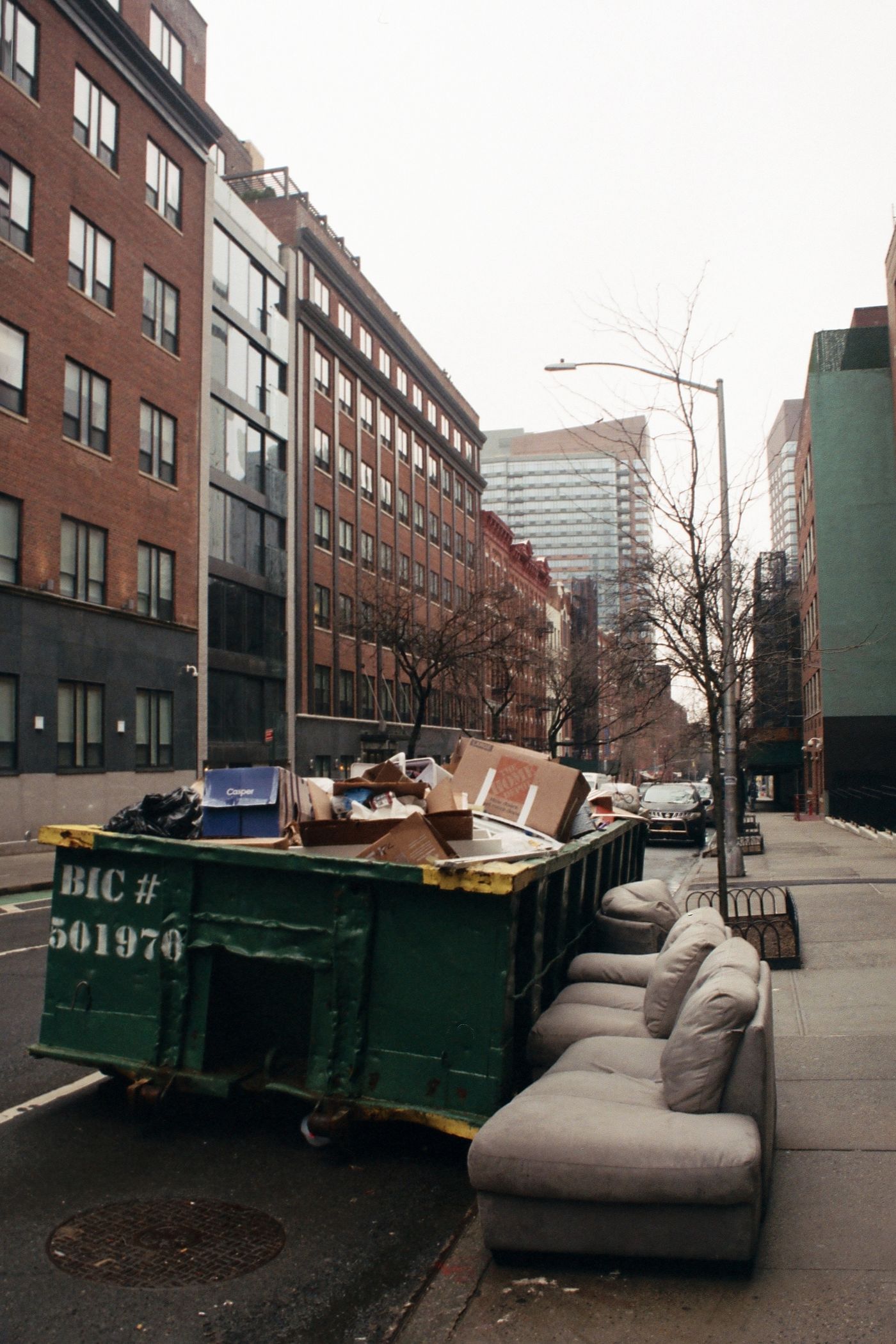 Dumpster loaded with junk beside a couch on the sidewalk